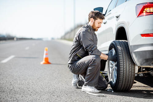 Roadside assistance putting a spare tire on a car.
